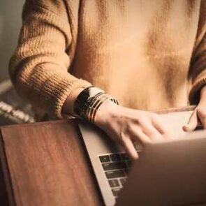 Close-up of a person's hands typing on a laptop, researching F.A.Qs about furniture and recliner repair.