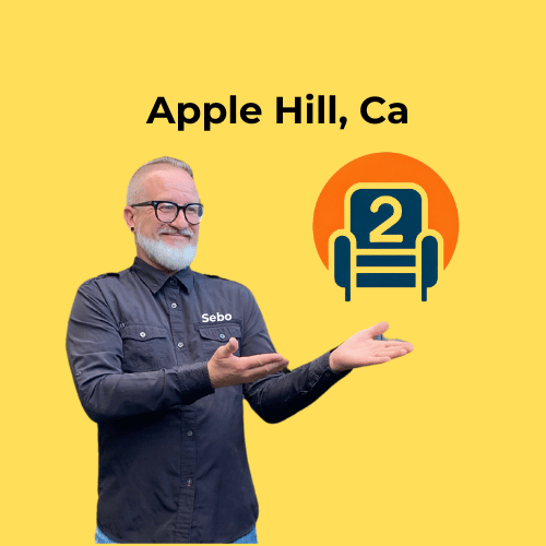 Sebastian in a dark Number2project shirt, smiling and pointing at a recliner logo with "Apple Hill, CA" on a yellow background.