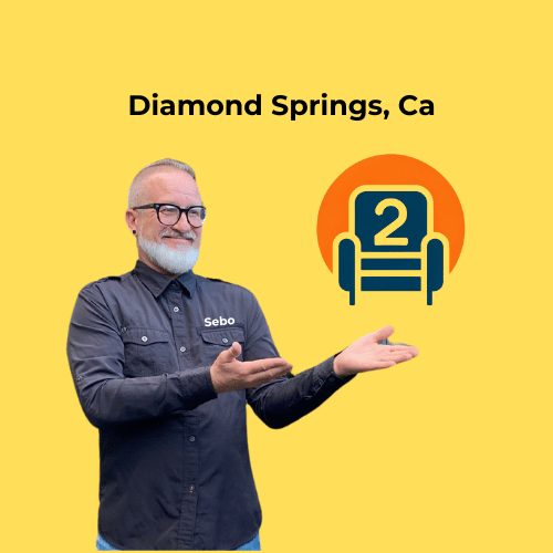 Sebastian in a dark Number2project shirt, smiling and pointing at a recliner logo with "Diamond Springs, CA" on a bright yellow background.